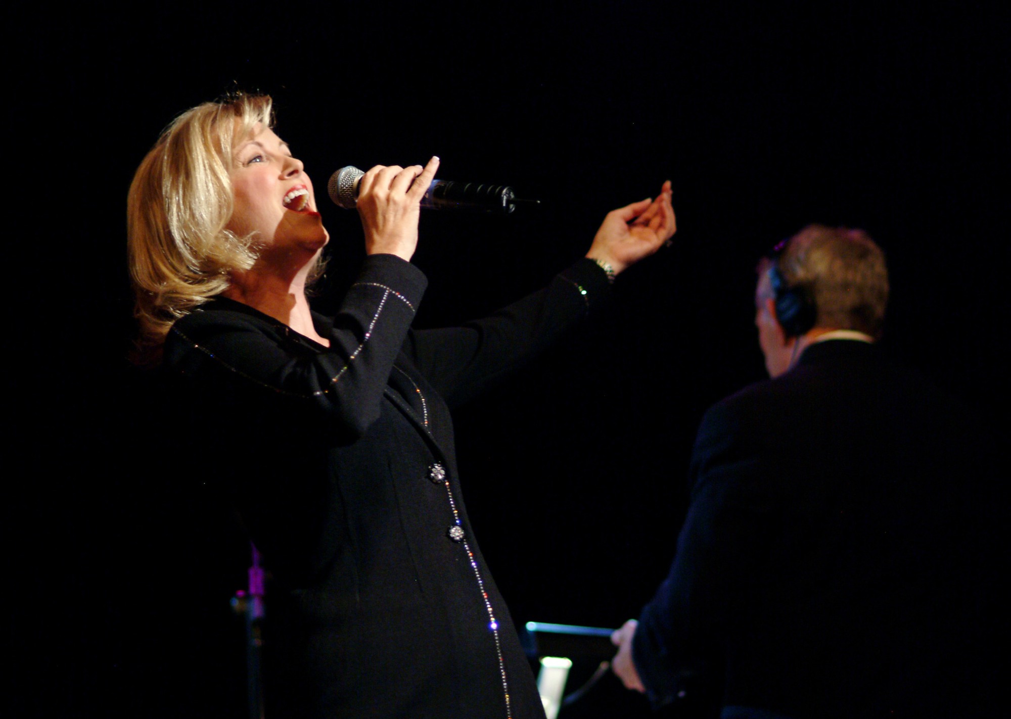 Laurie singing into a microphone on a dark concert stage
